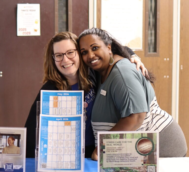 A library staff member and a foundation member pose together behind an information table.